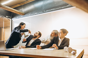 Image showing Angry boss with megaphone screaming at employees in office, scared and annoyed colleagues listening at the table