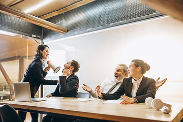 Image showing Angry boss with megaphone screaming at employees in office, scared and annoyed colleagues listening at the table