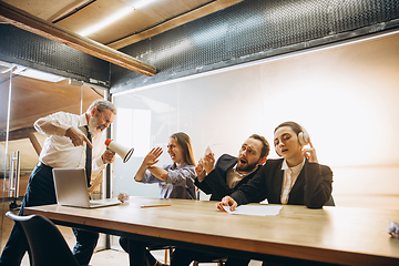 Image showing Angry boss with megaphone screaming at employees in office, scared and annoyed colleagues listening at the table