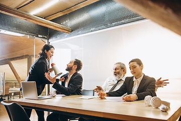 Image showing Angry boss with megaphone screaming at employees in office, scared and annoyed colleagues listening at the table