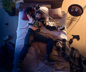 Image showing Top view of young professional hockey player sleeping at his bedroom in sportwear with equipment