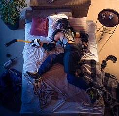 Image showing Top view of young professional hockey player sleeping at his bedroom in sportwear with equipment