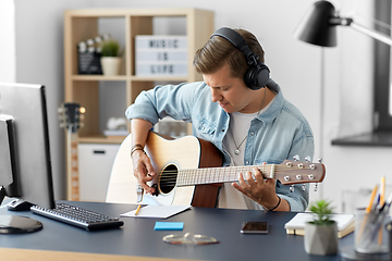 Image showing man in headphones playing guitar at home