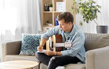 Image showing man with guitar writing to music book at home