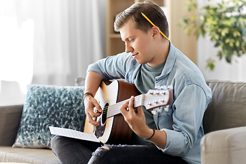 Image showing young man with music book playing guitar at home