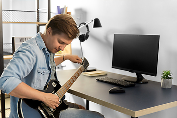 Image showing young man with computer playing guitar at home