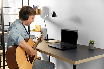 Image showing man in headphones playing guitar at home