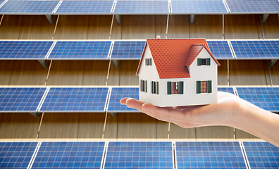 Image showing hand holding house model over solar panels