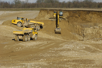 Image showing Yellow dump trucks and excavator are working in gravel pit