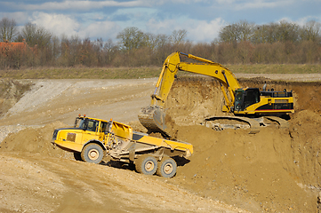 Image showing Yellow dump trucks and excavator are working in gravel pit