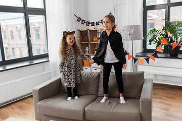 Image showing girls in halloween costumes jumping on sofa