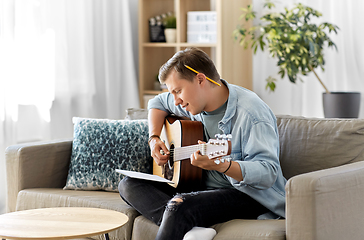 Image showing young man with music book playing guitar at home