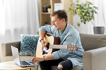 Image showing young man with laptop playing guitar at home