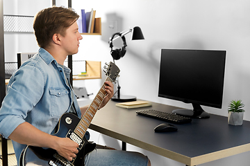 Image showing young man with computer playing guitar at home