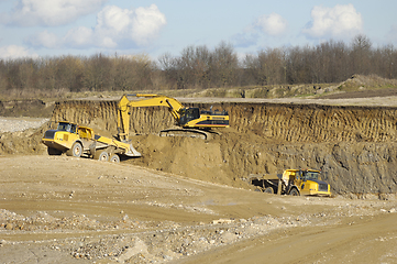 Image showing Yellow dump trucks and excavator are working in gravel pit