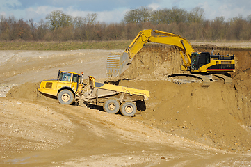 Image showing Yellow dump trucks and excavator are working in gravel pit