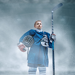 Image showing Little hockey player with the stick on ice court in smoke. Sportsboy wearing equipment and helmet training in action.