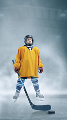 Image showing Little hockey player with the stick on ice court in smoke. Sportsboy wearing equipment and helmet training in action.