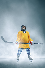 Image showing Little hockey player with the stick on ice court in smoke. Sportsboy wearing equipment and helmet training in action.