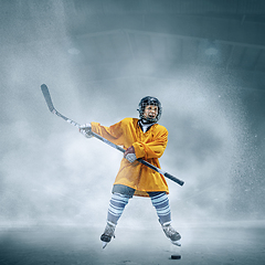 Image showing Little hockey player with the stick on ice court in smoke. Sportsboy wearing equipment and helmet training in action.