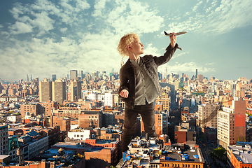 Image showing See the world by children\'s eyes - little cute curly boy playing with airplane standing in the city