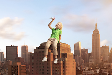 Image showing See the world by children\'s eyes - little cute curly boy playing with airplane sitting on the business centre