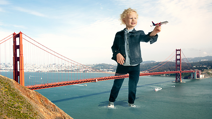 Image showing See the world by children\'s eyes - little cute curly boy playing with airplane standing on the bridge