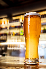 Image showing Glass of lager beer on wooden table in warm light of bar