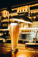 Image showing Glass of lager beer on wooden table in warm light of bar