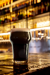 Image showing Glass of stout beer on wooden table in warm light of bar