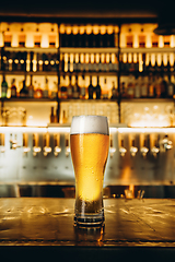 Image showing Glass of lager beer on wooden table in warm light of bar