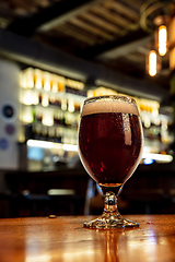 Image showing Glass of stout beer on wooden table in warm light of bar