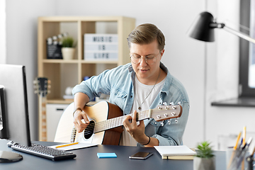 Image showing young man playing guitar sitting at table at home