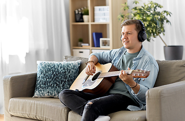 Image showing man in headphones playing guitar at home