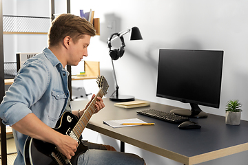 Image showing young man with music book playing guitar at home