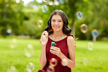 Image showing happy woman blowing soap bubbles at summer park