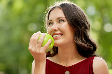 Image showing happy woman eating green apple at summer park