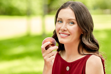 Image showing happy woman eating peach at summer park