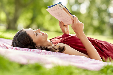 Image showing happy woman reading book lying on blanket at park