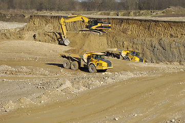 Image showing Yellow dump trucks and excavator are working in gravel pit