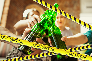 Image showing Close up hands clinking bottles of beer at bar with bounding tapes Lockdown, Coronavirus, Quarantine, Warning - closing bars and nightclubs during pandemic