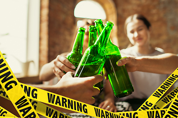 Image showing Close up hands clinking bottles of beer at bar with bounding tapes Lockdown, Coronavirus, Quarantine, Warning - closing bars and nightclubs during pandemic