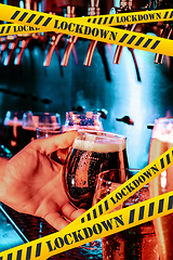 Image showing Hand of bartender pouring a beer in tap with bounding tapes Lockdown, Coronavirus, Quarantine, Warning - closing bars and nightclubs during pandemic