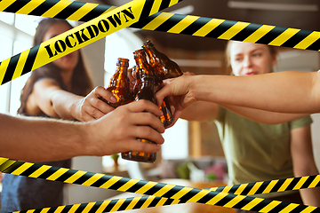 Image showing Close up hands clinking bottles of beer at bar with bounding tapes Lockdown, Coronavirus, Quarantine, Warning - closing bars and nightclubs during pandemic