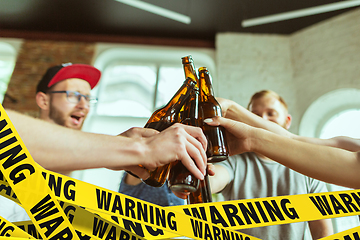 Image showing Close up hands clinking bottles of beer at bar with bounding tapes Lockdown, Coronavirus, Quarantine, Warning - closing bars and nightclubs during pandemic