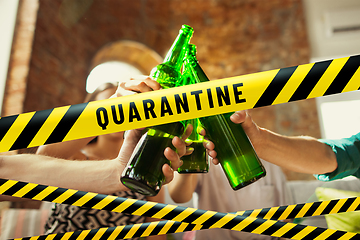 Image showing Close up hands clinking bottles of beer at bar with bounding tapes Lockdown, Coronavirus, Quarantine, Warning - closing bars and nightclubs during pandemic