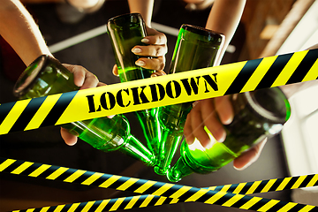 Image showing Close up hands clinking bottles of beer at bar with bounding tapes Lockdown, Coronavirus, Quarantine, Warning - closing bars and nightclubs during pandemic