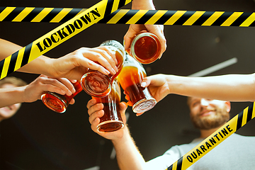 Image showing Close up hands clinking glasses of beer at bar with bounding tapes Lockdown, Coronavirus, Quarantine, Warning - closing bars and nightclubs during pandemic