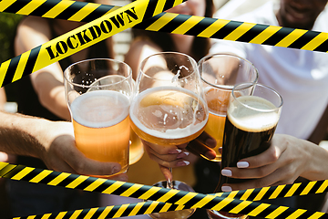 Image showing Close up hands clinking glasses of beer at bar with bounding tapes Lockdown, Coronavirus, Quarantine, Warning - closing bars and nightclubs during pandemic