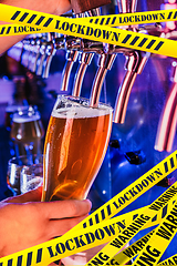 Image showing Hand of bartender pouring a beer in tap with bounding tapes Lockdown, Coronavirus, Quarantine, Warning - closing bars and nightclubs during pandemic